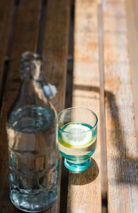 Glasflasche mit Wasser und Trinkglas mit einer Zitrone auf einem Holztisch